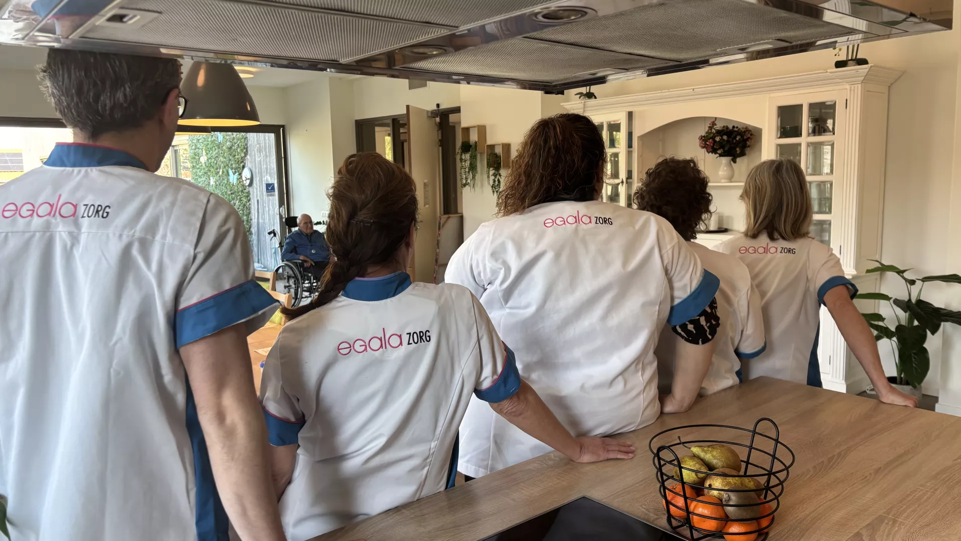 Zorgmedewerkers in een keuken in de rij met hun rug naar de camera.