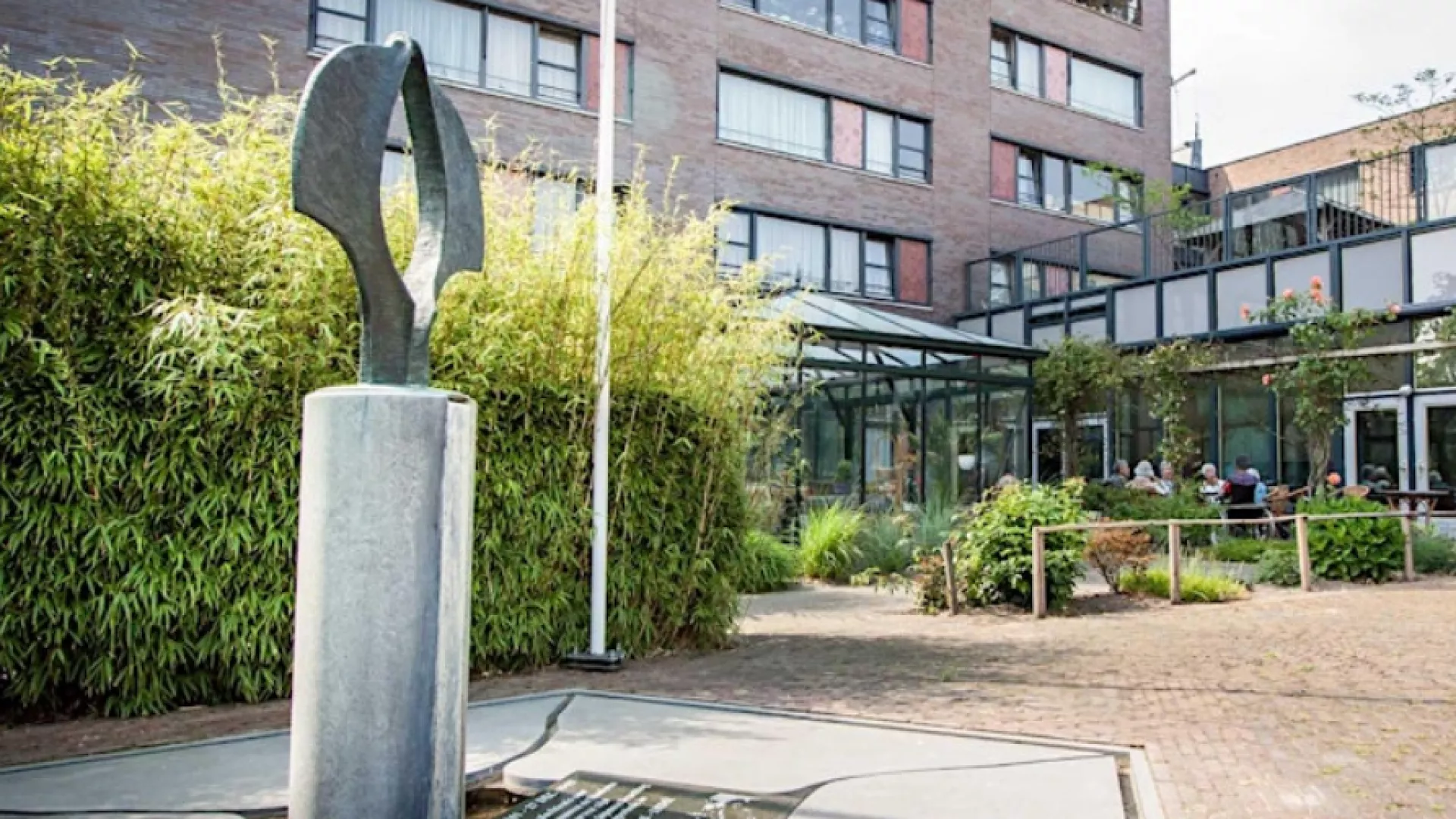 Een modern beeldhouwwerk voor een gebouw met glazen en bakstenen elementen.