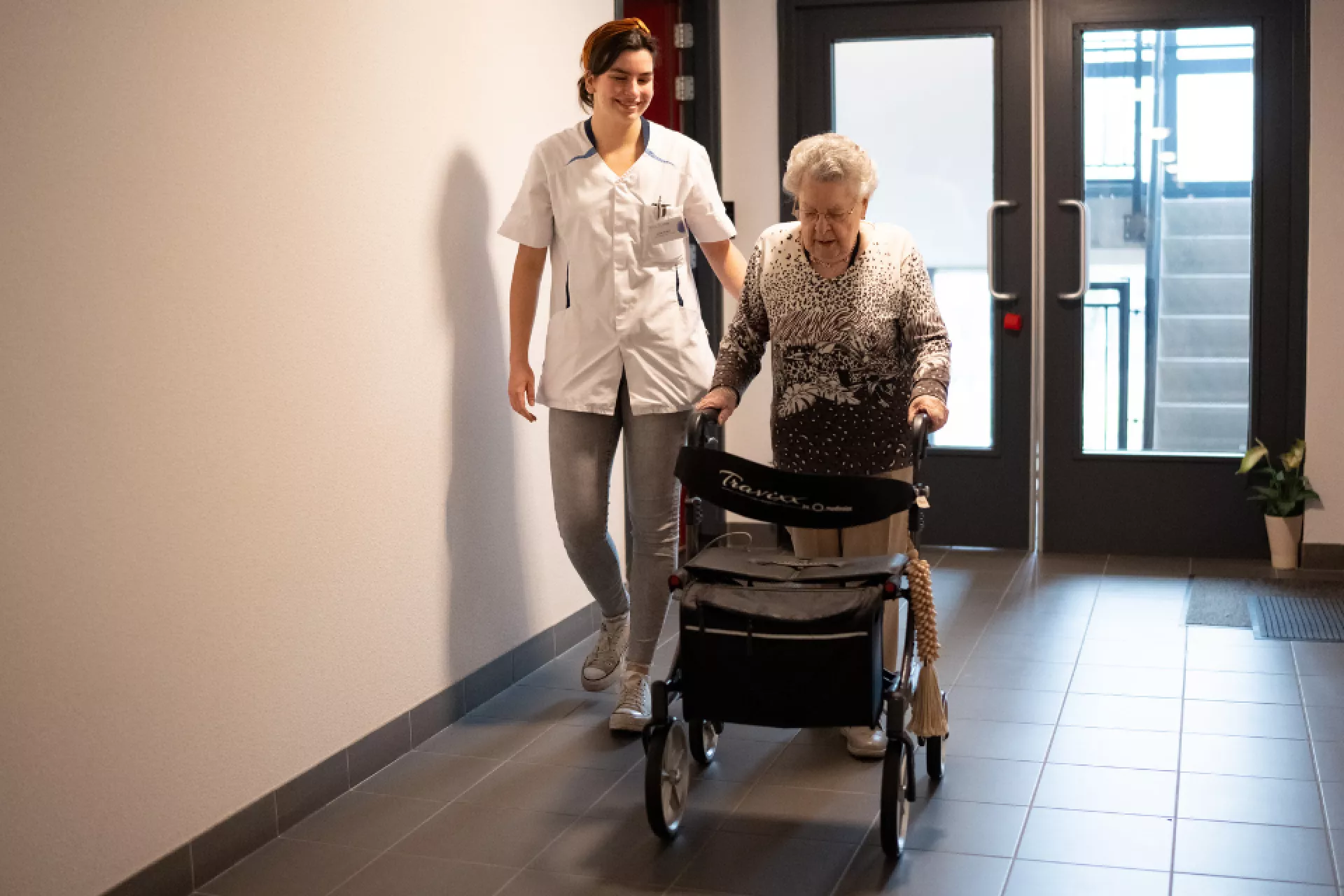 Thuiszorgmedewerker en client wandelen samen op gang